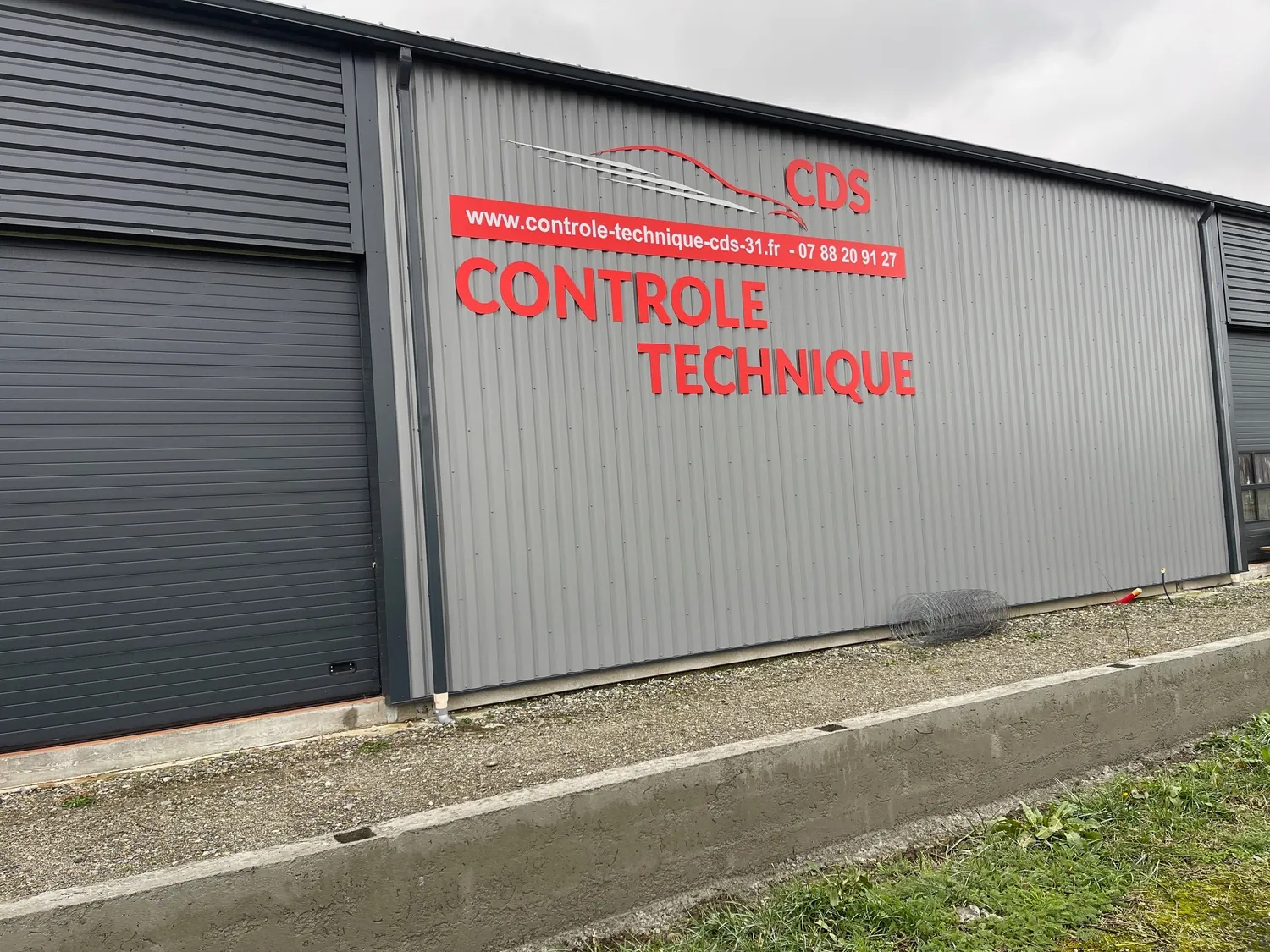 Enseigne CDS Contrôle Technique avec lettres rouges fixées sur un bâtiment métallique